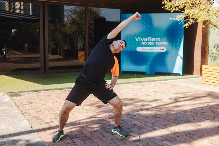 Na sequência, traga o braço direito para cima da cabeça, flexionando o quadril junto durante o movimento.