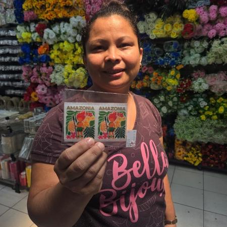 A vendedora Vanderly Rodrigues mostra os adesivos DTF do Curupira na loja Bella Bijoux A vendedora Vanderly Rodrigues mostra os adesivos DTF do Curupira na loja Bella Bijoux
