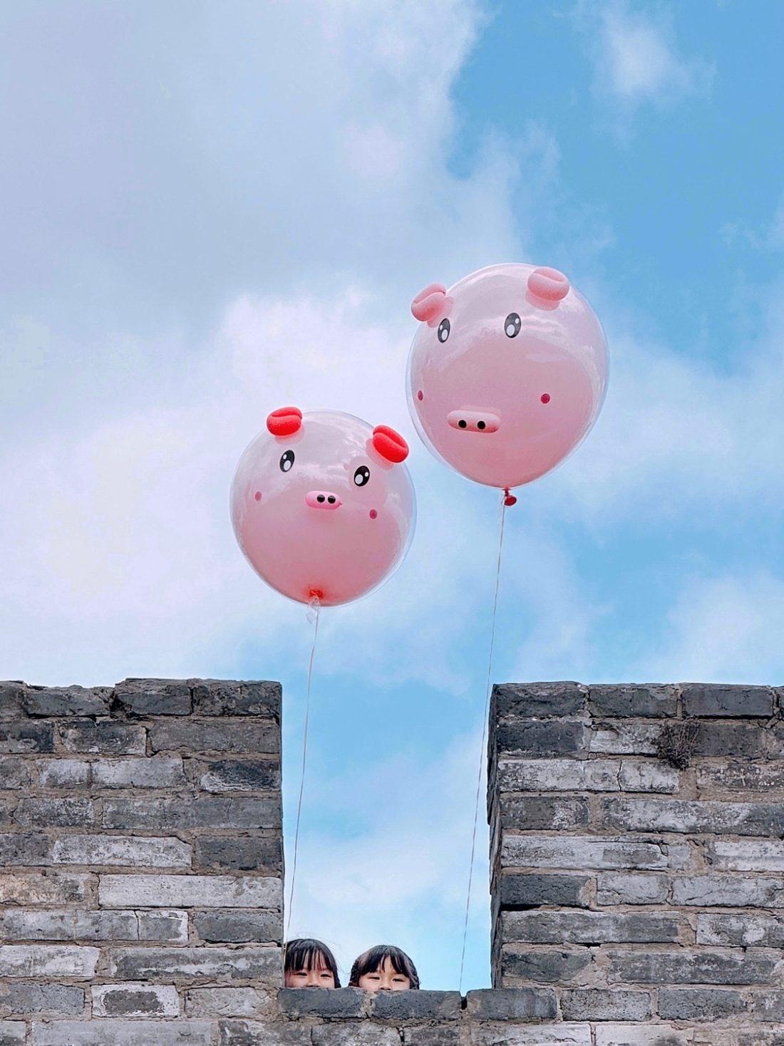 2º lugar da categoria Crianças: imagem destaca duas crianças segurando grandes balões de porquinho espionando por trás de um muro. O registro foi feito por Zhang Xiaojun com um iPhone 14 Pro Max, em Linhai Zhejiang. - Zhang Xiaojun/IPP Awards