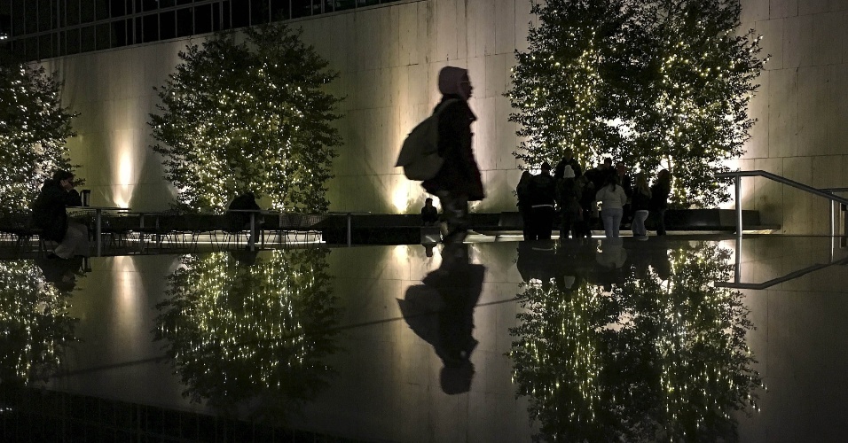 12.nov.2015 - Reflexo de pedestre aparece em uma superfície de pedra enquanto caminha junto a árvores iluminadas na cidade de Manhattan, em Nova York (EUA)