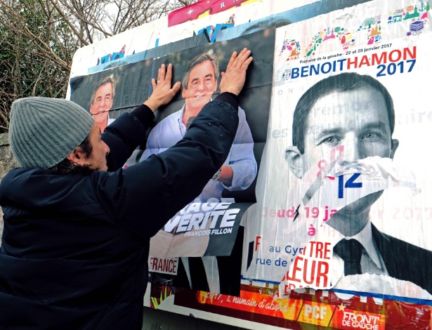 Homem cola cartazes do candidato da direita, François Fillon, sobre os do candidato socialista, Benoit Hamon, em Marselha, na França - Boris Horvat/AFP