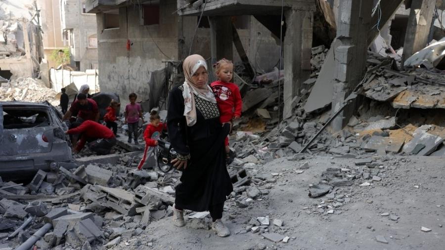 22.mai.2025 - Mulher e crianças palestinas andam em meio a escombros após ataques israelenses em Jabalia, no norte da Faixa de Gaza 22.mai.2025 - Mulher e crianças palestinas andam em meio a escombros após ataques israelenses em Jabalia, no norte da Faixa de Gaza
