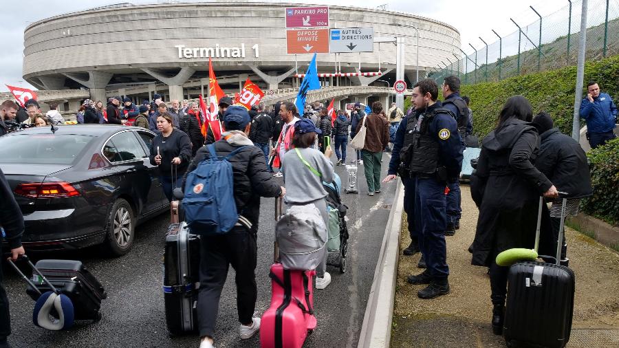 23.mar.23 - Passageiros caminham na estrada com suas bagagens enquanto funcionários do aeroporto em greve protestam do lado de fora do Terminal 1 no aeroporto Paris-Charles de Gaulle em Roissy, perto de Paris, França - Lucien Libert/Reuters