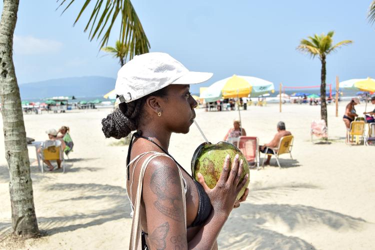 Banhista toma água de coco na praia do Itararé, em São Vicente, no litoral de São Paulo