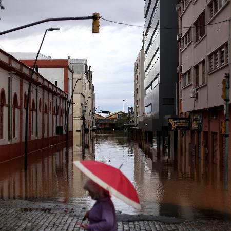 Pessoa anda de guarda-chuva por rua inundada no centro histórico de Porto Alegre (RS)