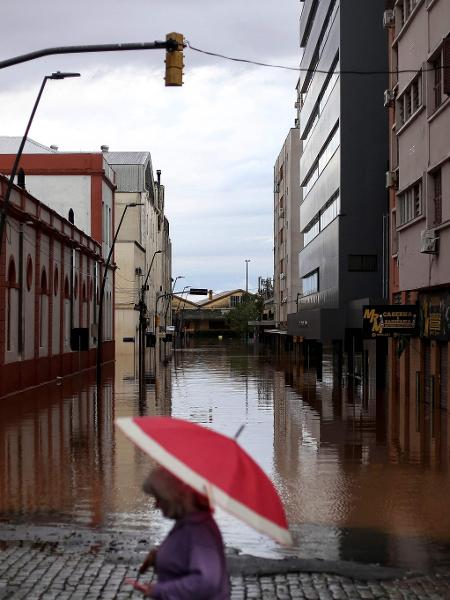 Pessoa anda de guarda-chuva por rua inundada no centro histórico de Porto Alegre