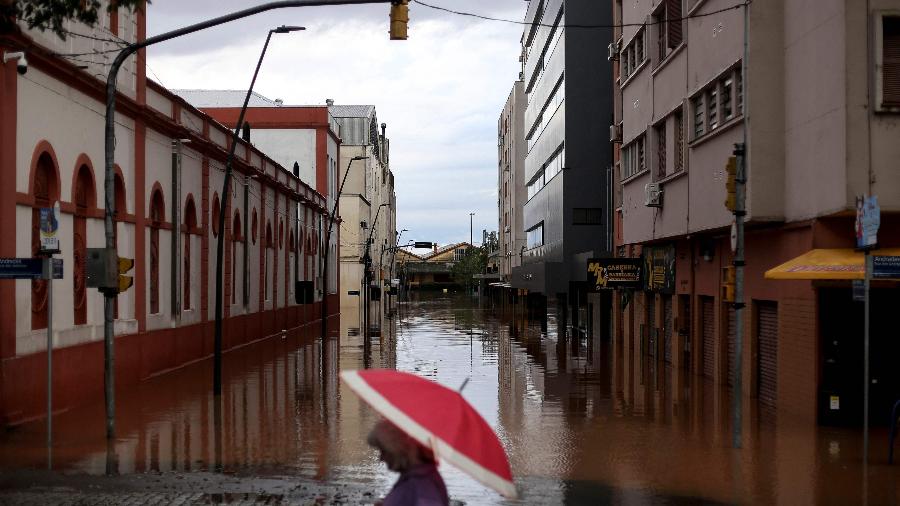 Pessoa anda de guarda-chuva por rua inundada no centro histórico de Porto Alegre (RS)