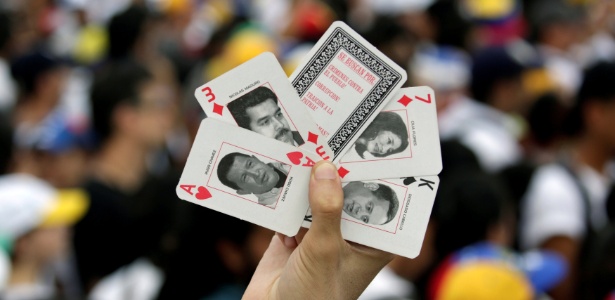 Manifestante mostra cartas de baralho com as imagens de Hugo Chávez e Nicolás Maduro durante protesto de opositores ao governo venezuelano, em Caracas