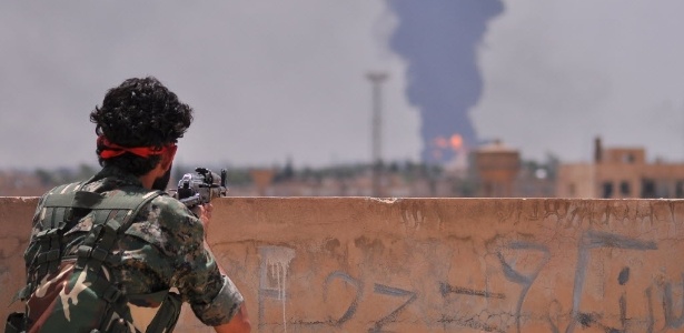 Membro da milícia sírio-curda Unidades de Proteção do Povo (YPG) aponta arma em direção a região bombardeada de Hasakah - Delil Souleiman/AFP