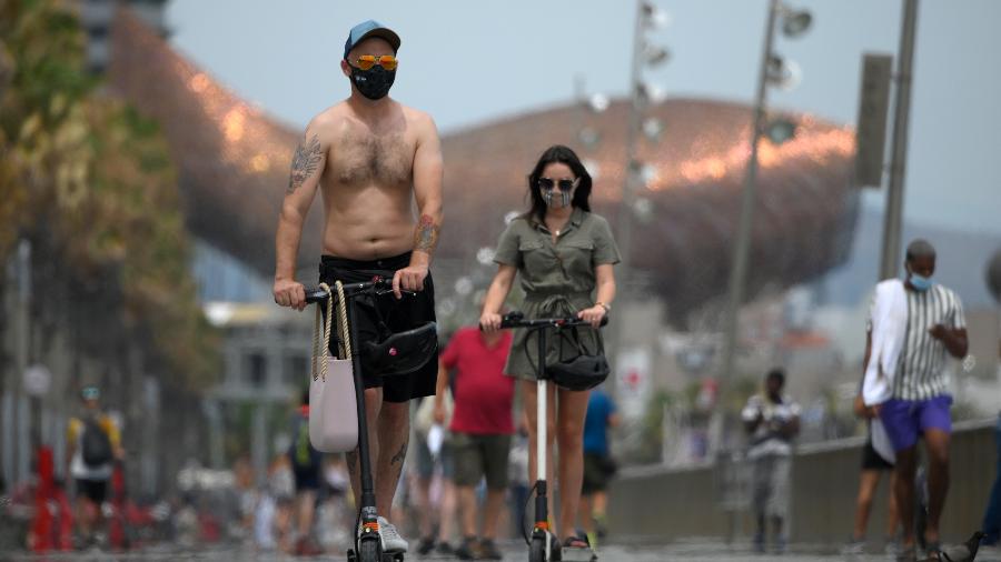 De máscara, moradores andam de patinete próximo à praia de Barceloneta, em Barcelona, na Espanha - Lluis Gene/AFP