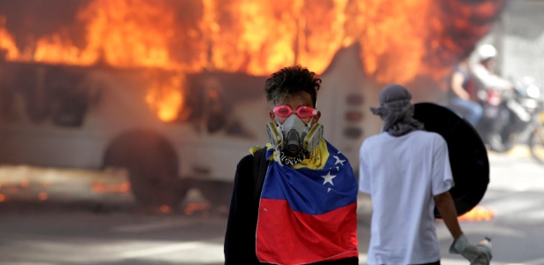 Manifestante posa para foto diante de ônibus em chamas durante protesto contra o governo de Nicolás Maduro, em Caracas - Christian Veron/ Reuters