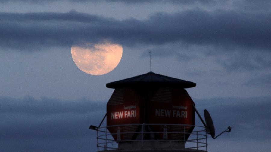 Lua cheia ganha tom rosado ao lado de um farol em Tirana, na Albânia - Florion Goga/Reuters