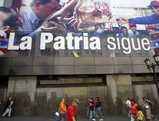 Pedestres passam por propaganda com os presidentes Nicolás Maduro e Hugo Chávez, próximo à Assembleia Nacional em Caracas, na Venezuela - Carlos Garcia Rawlins/Reuters