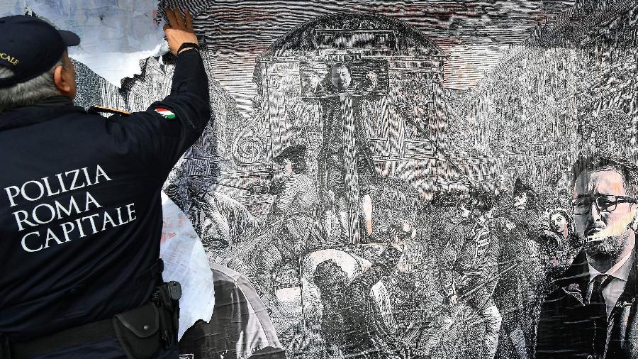 Policial remove poster colocado em uma banca de jornais em Roma mostrando Cesare Battisti (ao centro) no pelourinho - Alberto Pizzoli/AFP