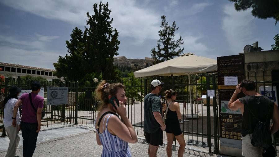 Turistas ficam do lado de fora da antiga Ágora fechada sob a colina da Acrópole, durante um dia quente em Atenas em 13 de junho de 2024