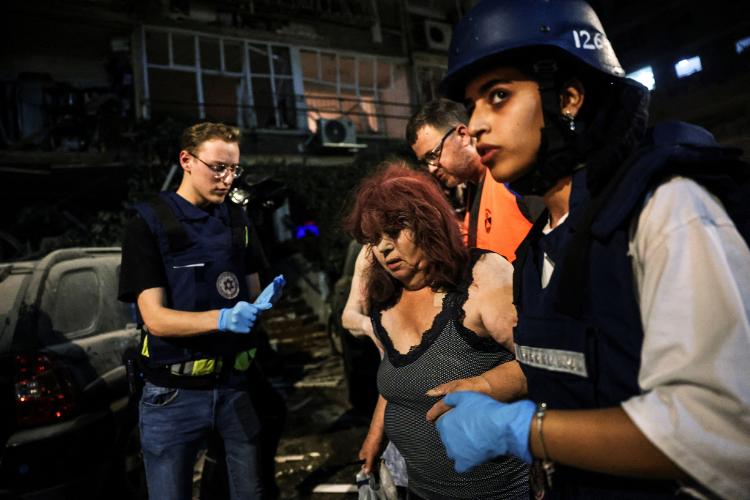 15.6.2025 - Equipe de resgate ajuda uma mulher ferida no local do impacto após ataque de míssil do Irã contra Israel 15.6.2025 - Equipe de resgate ajuda uma mulher ferida no local do impacto após ataque de míssil do Irã contra Israel