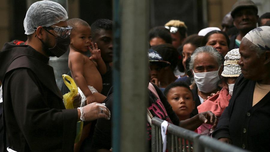 Um frade franciscano é visto com pessoas que se reúnem para receber doação de alimentos ao lado do convento de São Francisco, durante o surto da doença por coronavírus, em São Paulo - RAHEL PATRASSO/REUTERS