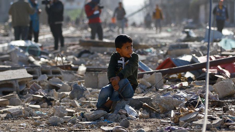 Criança palestina sentada entre os escombros de casas destruídas num ataque israelense em Khan Younis, no sul da Faixa de Gaza.