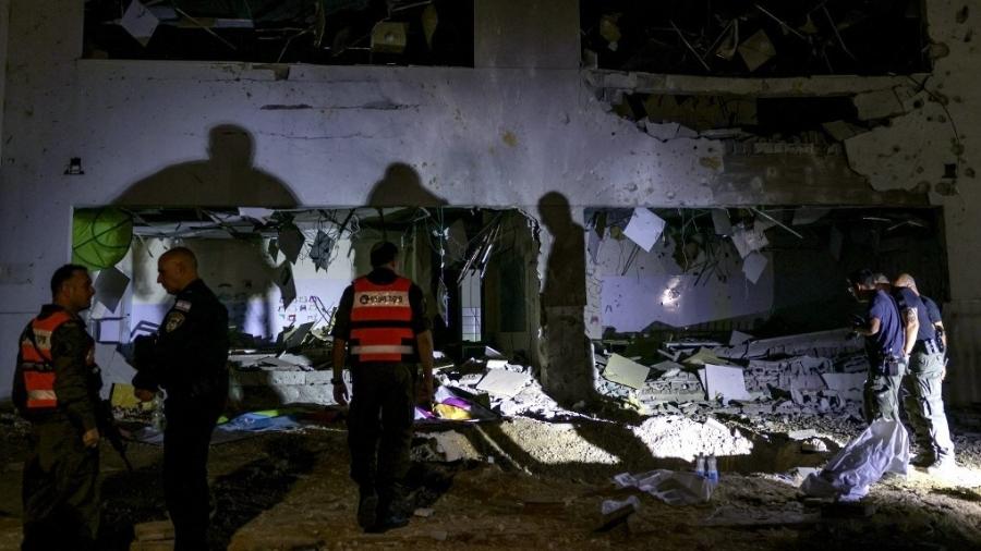 Membros do Comando da Frente Interna de Israel e forças policiais inspecionam uma cratera deixada por um projétil explodido em um prédio escolar na cidade de Gedera, no sul de Israel, depois que o Irã lançou mísseis contra Israel