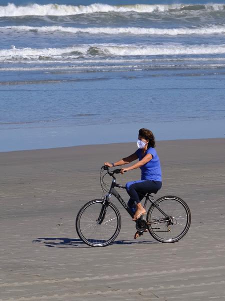 29.mai.2020 - De máscara, moradora anda de bicicleta na praia da Baleia, em São Sebastião, litoral norte de São Paulo - Marcello Zambrana/AGIF/Estadão Conteúdo