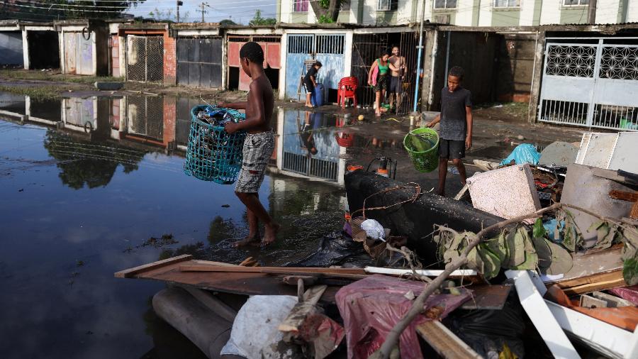 14.jan.2024 - Crianças coletam pertences após fortes chuvas que atingiram o Complexo da Pedreira, no Rio