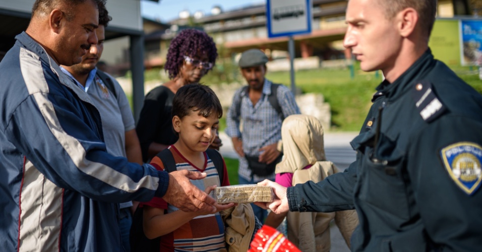 18.set.2015 - Policial croata oferece comida e água a migrantes na fronteira com a Eslovênia. O ministro do Interior da Croácia, Ranko Ostojic, declarou nesta sexta-feira (18) que a capacidade de recepção do país está "saturada", depois que 13 mil migrantes entraram no país em dois dias