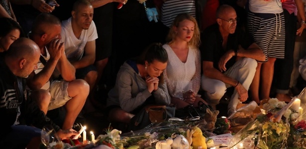 Pessoas rezam em torno de memorial improvisado para homenagear as vítimas do ataque com caminhão na cidade francesa de Nice - Valery Hache/ AFP