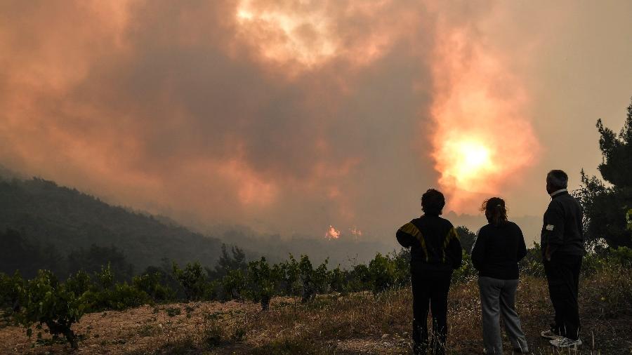 Residentes locais observam um incêndio florestal perto da vila de Pefkaneas, a oeste de Atenas, na Grécia. - Louisa GOULIAMAKI / AFP