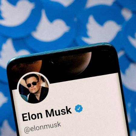 Perfil de Elon Musk no Twitter exibido em um celular com logotipos da rede social ao fundo - Dado Ruvic/Reuters