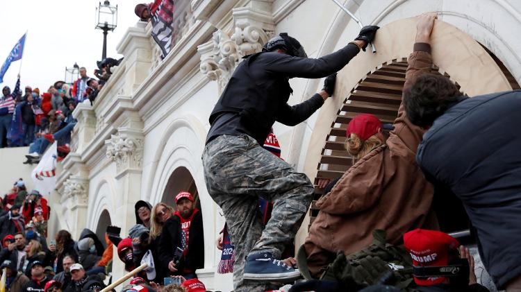 Manifestantes pró-Trump escalam um muro enquanto invadem o Capitólio dos EUA, durante confrontos com a polícia em 6 de janeiro de 2021