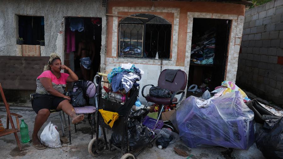 14.jan.2024 - Mulher sentada no lado de fora da sua casa com seus pertences após fortes chuvas que atingiram o Complexo da Pedreira, na cidade do Rio de Jnaeiro