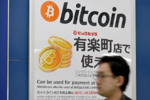 Homem passa por cartaz anunciando que bitcoin é aceita como forma de pagamento em loja de Tóquio (Japão) - Toru Yamanaka/AFP