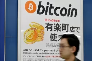 Homem passa por cartaz anunciando que bitcoin é aceita como forma de pagamento em loja de Tóquio (Japão) - Toru Yamanaka/AFP