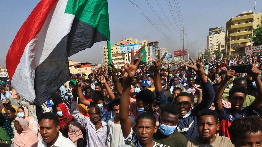 Manifestantes sudaneses erguem bandeiras enquanto se manifestam na capital Cartum, para denunciar as detenções noturnas do exército de membros do governo - AFP