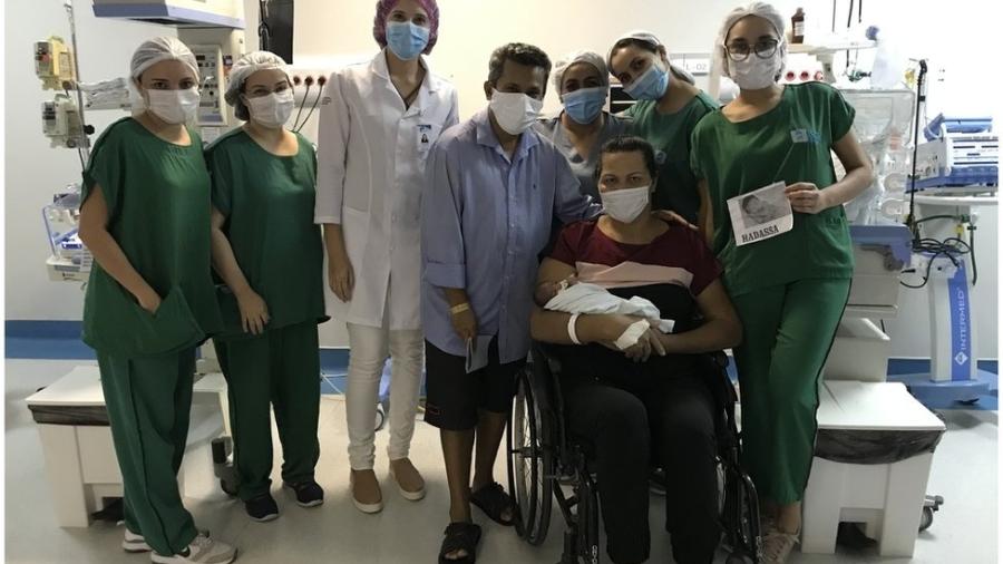 Lurdyani, na cadeira de rodas, ao lado do marido e da equipe médica, pega a filha no colo pela primeira vez, 51 dias depois do parto - Divulgação