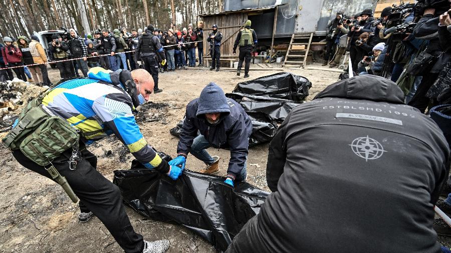 05.abr.2022 - Policiais e funcionários da cidade carregam seis corpos parcialmente queimados em sacos para corpos enquanto repórteres atendem na cidade de Bucha - GENYA SAVILOV / AFP