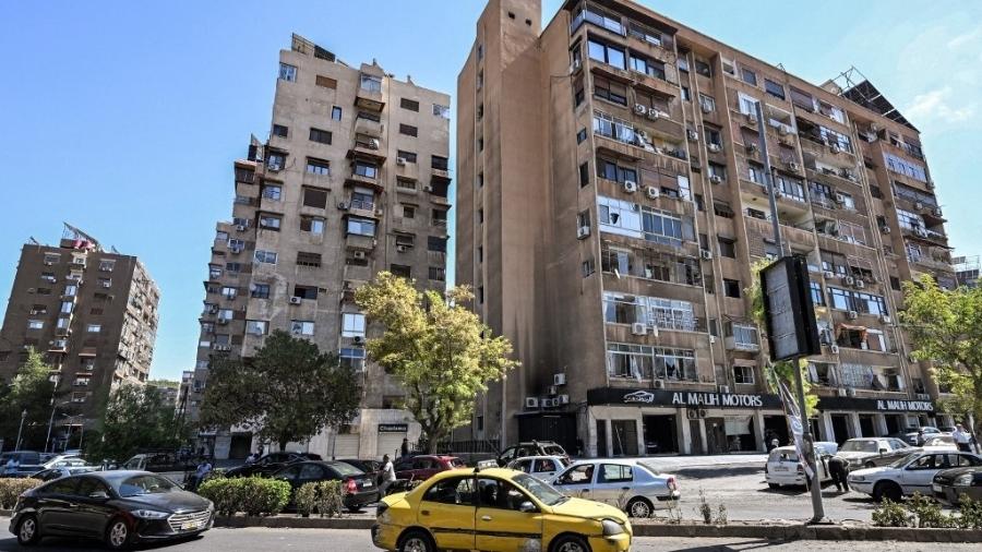 Veículos passam por prédios que foram danificados no bairro de Mazzeh, no leste de Damasco, após ataques aéreos israelenses contra a capital síria na manhã de 1º de outubro de 2024 - LOUAI BESHARA/AFP