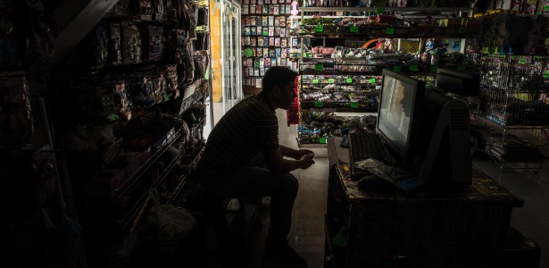Kevin Munoz espera por clientes no escuro em sua loja, durante apagão em Caracas, na Venezuela - Meridith Kohut/The New York Times