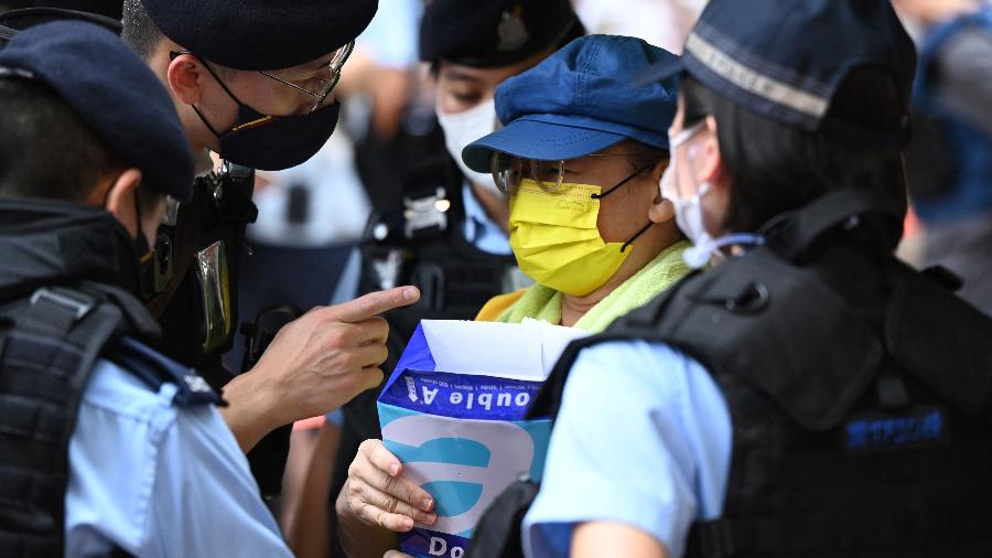 04.jun.22 - A polícia questiona uma mulher enquanto ela segura folhas de papel em branco no distrito de Causeway Bay, em Hong Kong, perto do local onde moradores se reúnem para lamentar as vítimas da repressão na Praça da Paz Celestial em 1989 - PETER PARKS/AFP