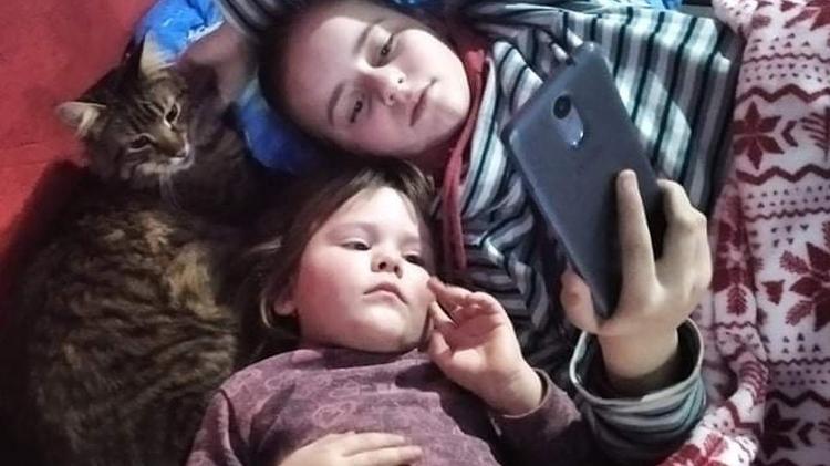 Yuliia's daughters watch a video on their mother's phone - BBC - BBC
