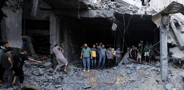 Civis palestinos procuram sobreviventes nos escombros de edifício atingido em bombardeio israelense em Khan Yunis, sul da Faixa de Gaza, nesta quinta (19)