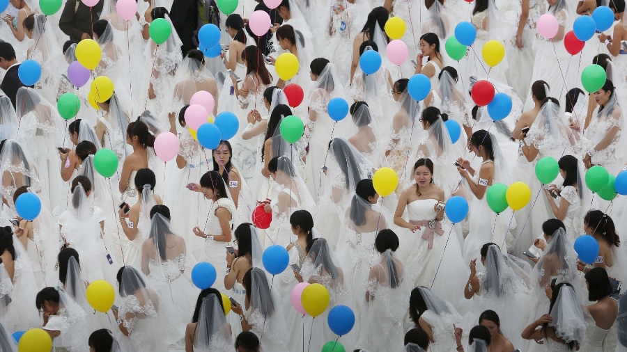 Mulheres de vestido de noiva seguram bexigas durante um evento de casamentos em Suzhou, na província de Jiangsu, China - China Daily/Reuters