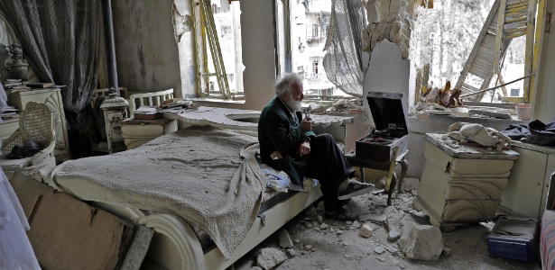 Mohammad Mohiedine Anis, 70, fuma seu cachimbo enquanto ouve música em seu quarto destruído em Aleppo - JOSEPH EID/AFP
