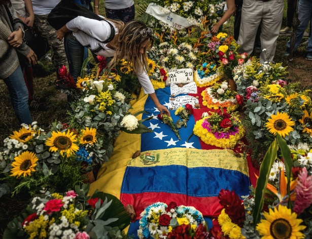 Mulher coloca flores no túmulo do líder rebelde Óscar Perez, em El Hatillo, na Venezuela - Meridith Kohut/The New York Times