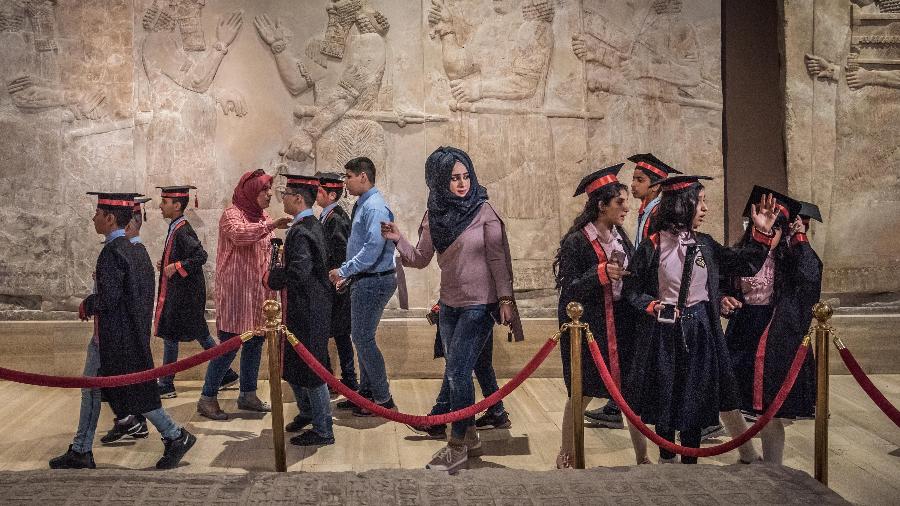 Visitantes do Museu do Iraque, em Bagdá, passam em frente a murais assírios - Sergey Ponomarev/The New York Times