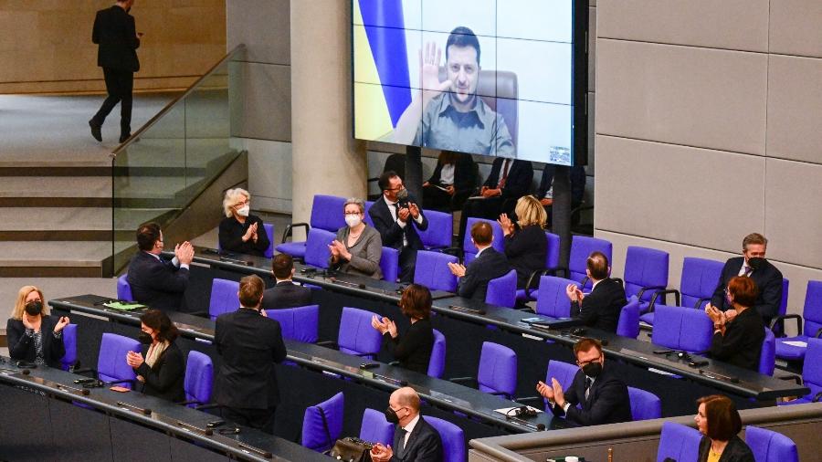 Membros do governo alemão, entre eles o chanceler alemão Olaf Scholz, aplaudem quando o presidente ucraniano Volodymyr Zelensky aparece em uma tela para abordar via vídeo a Câmara Baixa do Parlamento alemão Bundestag - Tobias Schwarz/AFP