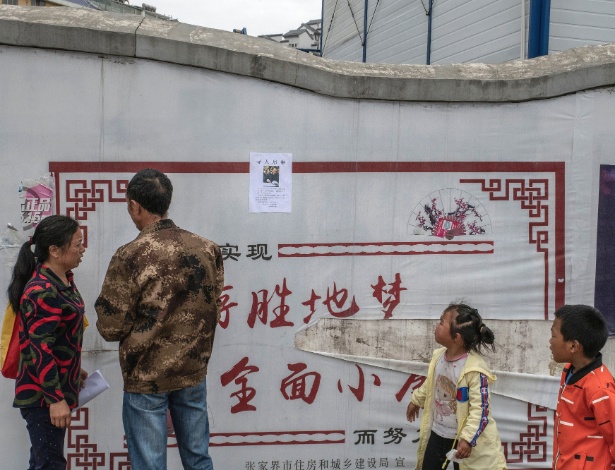 Liao Mandong, à esquerda, e Tang Chunwu, segundo à esquerda, colocaram cartazes para ajudar na busca por seu filho Tang Gongwei, um farmacêutico de 26 anos que desapareceu após ser diagnosticado com câncer de estômago, em Zhangjiajie, China - Gilles Sabrié/The New York Times