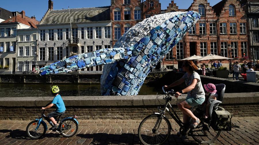 Ciclistas passam por escultura de baleia feita de lixo plástico, em exibição na Bélgica para a Trienal de Bruges, em 2018 - John Thys/Agence France-Presse/Getty Images