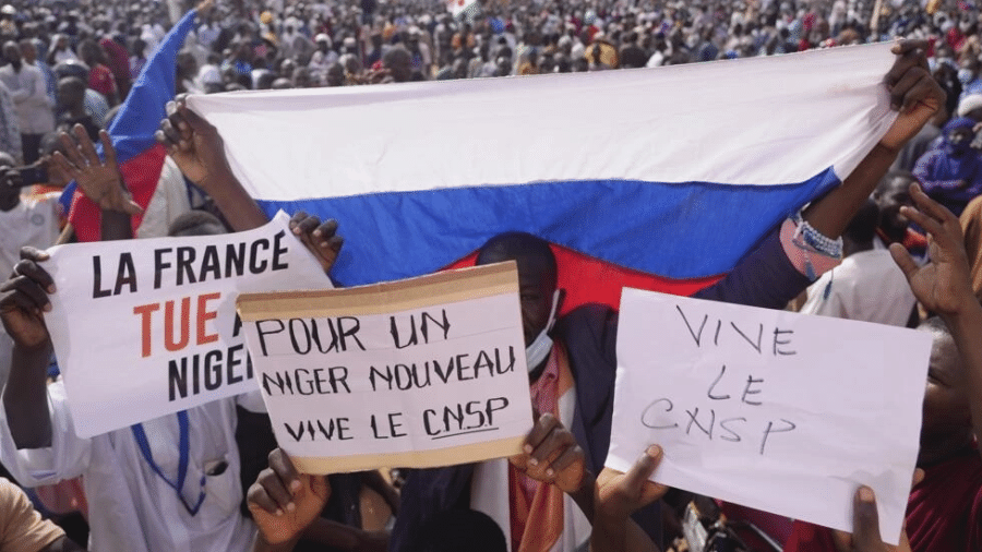 Manifestantes favoráveis ao golpe militar exibem a bandeira da Rússia e cartazes com as frases 'França assassina' e 'Por um novo Níger', durante protesto nas ruas de Niamey
