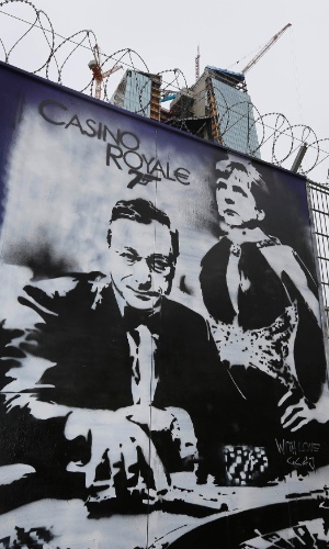 16.mai.13 - Um grafite feito em um muro perto de onde será construída a nova sede do Banco Central Europeu (BCE) em Frankfurt (Alemanha) mostra o presidente do banco, Mario Draghi, e a chanceler da Alemanha, Angela Merkel, simulando uma cena do filme "Casino Royale"